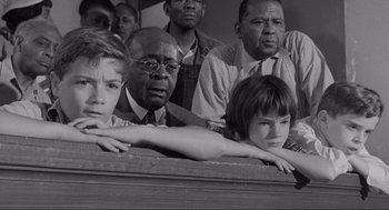 Movie still from “To Kill a Mockingbird” (1962), directed by Robert Mulligan – A black and white photo of a group of people sitting on a bench; Medium shot, High angle