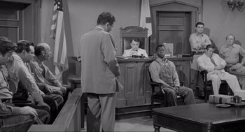 Movie still from “To Kill a Mockingbird” (1962), directed by Robert Mulligan – Two men in a courtroom , one of whom is sitting on a bench; Medium shot, Over the shoulder angle