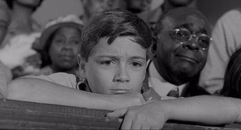 Movie still from “To Kill a Mockingbird” (1962), directed by Robert Mulligan – A young boy sitting in front of a group of people; Close Up shot, High angle