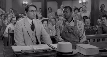 Movie still from “To Kill a Mockingbird” (1962), directed by Robert Mulligan – Two men sitting at a table in front of a group of people; Medium shot, Low angle