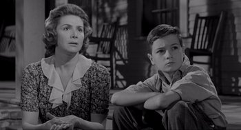 Movie still from “To Kill a Mockingbird” (1962), directed by Robert Mulligan – A woman sitting next to a young boy in front of a chair; Medium shot, Low angle
