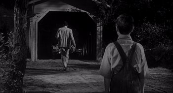 Movie still from “To Kill a Mockingbird” (1962), directed by Robert Mulligan – A man walking down a dirt road while holding a camera; Wide shot, Over the shoulder angle