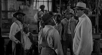 Movie still from “To Kill a Mockingbird” (1962), directed by Robert Mulligan – A black and white photo of a group of men in hats and overalls; Medium shot, Over the shoulder angle
