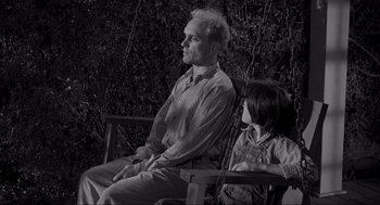 Movie still from “To Kill a Mockingbird” (1962), directed by Robert Mulligan – An older man sitting on a swing next to a young girl; Medium shot, Low angle