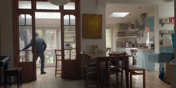Movie still from “Together” (2021), directed by Justin Martin – A dining room with a table , chairs and a painting on the wall; Wide shot, Low angle