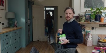 Movie still from “Together” (2021), directed by Justin Martin – A man sitting in front of a doorway holding a bag of food; Medium shot, Over the shoulder angle