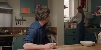 Movie still from “Together” (2021), directed by Justin Martin – A man sitting at a table in a kitchen; Medium shot, Over the shoulder angle