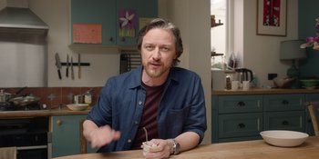 Movie still from “Together” (2021), directed by Justin Martin – A man sitting at a table with a cup in his hand; Medium shot, Low angle