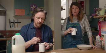 Movie still from “Together” (2021), directed by Justin Martin – A man and a woman sitting at a wooden table with coffee cups; Medium shot, Low angle