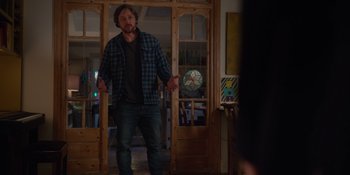 Movie still from “Together” (2021), directed by Justin Martin – A man standing in front of a room with wooden doors; Medium shot, Over the shoulder angle