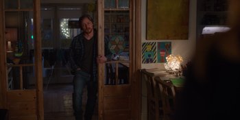 Movie still from “Together” (2021), directed by Justin Martin – A man standing in a room next to a table; Wide shot, Over the shoulder angle