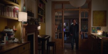Movie still from “Together” (2021), directed by Justin Martin – A man standing in front of an open door in a room; Wide shot, Low angle