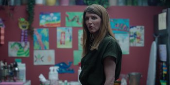 Movie still from “Together” (2021), directed by Justin Martin – A woman standing in front of a wall with pictures on it; Medium shot, Over the shoulder angle