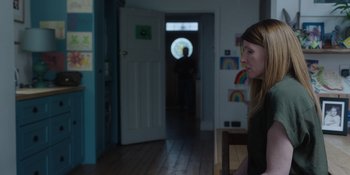 Movie still from “Together” (2021), directed by Justin Martin – A woman standing in front of an open door; Medium shot, Over the shoulder angle