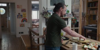 Movie still from “Together” (2021), directed by Justin Martin – A man standing at a table in a room; Medium shot, Over the shoulder angle