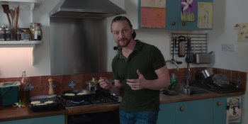 Movie still from “Together” (2021), directed by Justin Martin – A man standing in front of a stove cooking food; Medium shot, Low angle