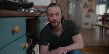 Movie still from “Together” (2021), directed by Justin Martin – A person sitting in a room near a stove; Close Up shot, Low angle