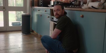 Movie still from “Together” (2021), directed by Justin Martin – A man sitting on the floor in front of a kitchen counter; Medium shot, Over the shoulder angle