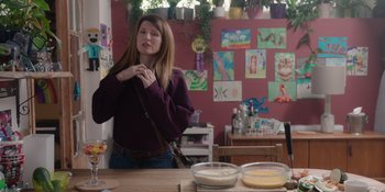Movie still from “Together” (2021), directed by Justin Martin – A woman standing at a table holding a purse; Medium shot, Over the shoulder angle