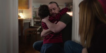 Movie still from “Together” (2021), directed by Justin Martin – A man and a child hugging in a living room; Medium shot, Over the shoulder angle