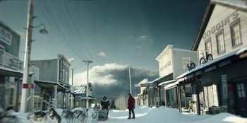 Movie still from “Togo” (2019), directed by Ericson Core – A person standing on a snow covered street near buildings; Extreme Wide shot, Low angle