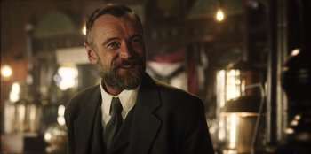 Movie still from “Togo” (2019), directed by Ericson Core – A man in a suit and tie smiling for the camera; Close Up shot, Low angle