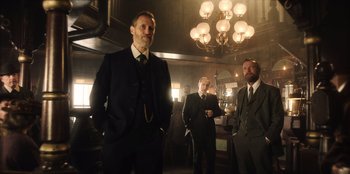 Movie still from “Togo” (2019), directed by Ericson Core – A group of men in suits standing in a dimly - lit room; Medium shot, Low angle