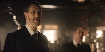 Movie still from “Togo” (2019), directed by Ericson Core – A man in a suit and tie standing next to another man in a suit and tie; Close Up shot, Low angle