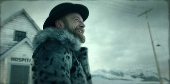 Movie still from “Togo” (2019), directed by Ericson Core – A man with a beard wearing a fur coat and a hat; Medium shot, Low angle