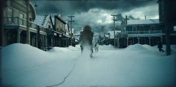 Movie still from “Togo” (2019), directed by Ericson Core – A man walking down a snow covered street with a dog; Wide shot, Low angle