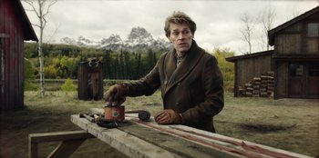 Movie still from “Togo” (2019), directed by Ericson Core – A man in a brown jacket is standing at a picnic table; Medium shot, Low angle