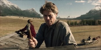 Movie still from “Togo” (2019), directed by Ericson Core – A man holding an axe while standing next to another man; Medium shot, Low angle