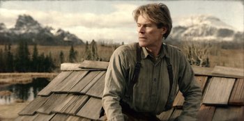 Movie still from “Togo” (2019), directed by Ericson Core – A man sitting on top of a wooden roof; Medium shot, Low angle