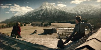 Movie still from “Togo” (2019), directed by Ericson Core – Two people are sitting on the porch of a ranch; Extreme Wide shot, High angle