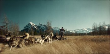 Movie still from “Togo” (2019), directed by Ericson Core – A man on a bike with a bunch of dogs in the background; Extreme Wide shot, High angle