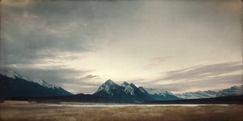 Movie still from “Togo” (2019), directed by Ericson Core – A view of a mountain range from across a field; Extreme Wide shot, High angle