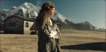 Movie still from “Togo” (2019), directed by Ericson Core – A woman standing in front of a house in a field; Medium shot, Low angle