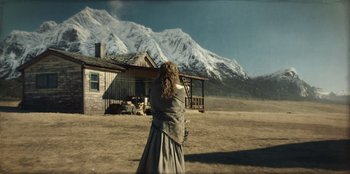 Movie still from “Togo” (2019), directed by Ericson Core – A woman standing in front of a house in the desert; Wide shot, Low angle