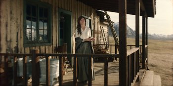 Movie still from “Togo” (2019), directed by Ericson Core – A woman standing on the porch of a log cabin; Wide shot, Low angle