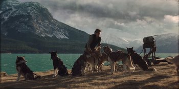 Movie still from “Togo” (2019), directed by Ericson Core – A man standing next to a group of dogs; Wide shot, Low angle