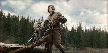 Movie still from “Togo” (2019), directed by Ericson Core – A man with a large backpack walking across a forest; Wide shot, Low angle