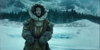 Movie still from “Togo” (2019), directed by Ericson Core – A man in a fur coat standing in the middle of a snow covered field; Medium shot, Low angle
