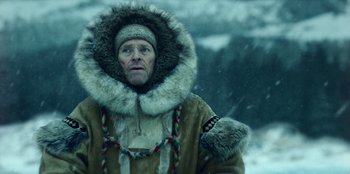 Movie still from “Togo” (2019), directed by Ericson Core – A man wearing a fur coat and a fur hat in the snow; Close Up shot, Low angle