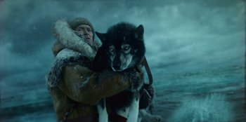 Movie still from “Togo” (2019), directed by Ericson Core – A man holding a dog in his arms in the middle of the ocean; Medium shot, Low angle