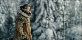 Movie still from “Togo” (2019), directed by Ericson Core – A man in a fur lined coat standing in front of a snowy mountain; Medium shot, Low angle