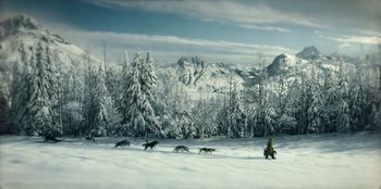 Movie still from “Togo” (2019), directed by Ericson Core – A man sitting in the snow with a pack of sled dogs; Extreme Wide shot, High angle