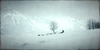 Movie still from “Togo” (2019), directed by Ericson Core – A person is standing in the snow with a dog sled; Extreme Wide shot, Low angle