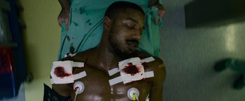 Movie still from “Without Remorse” (2021), directed by Stefano Sollima – A man in a hospital bed with bandages on his chest; Medium shot, Overhead angle