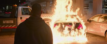 Movie still from “Without Remorse” (2021), directed by Stefano Sollima – A man standing in front of a car on fire; Wide shot, Over the shoulder angle
