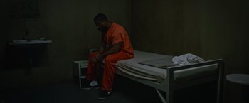Movie still from “Without Remorse” (2021), directed by Stefano Sollima – A man sitting on top of a bed in a jail cell; Wide shot, High angle
